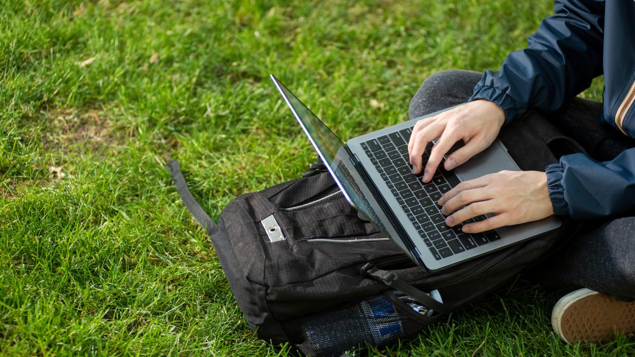 Student types on a laptop while sitting on green grass