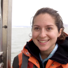 Meghan Holst, Ph.D. student, stands on a boat in the San Francisco Bay wearing an orange jacket next to a ladder
