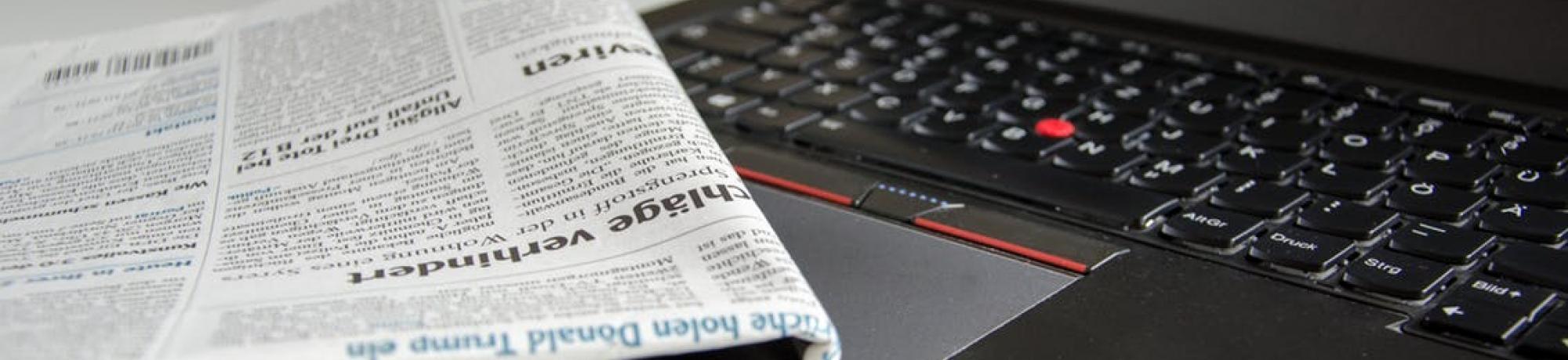 Newspaper rolled up and sitting on computer keyboard